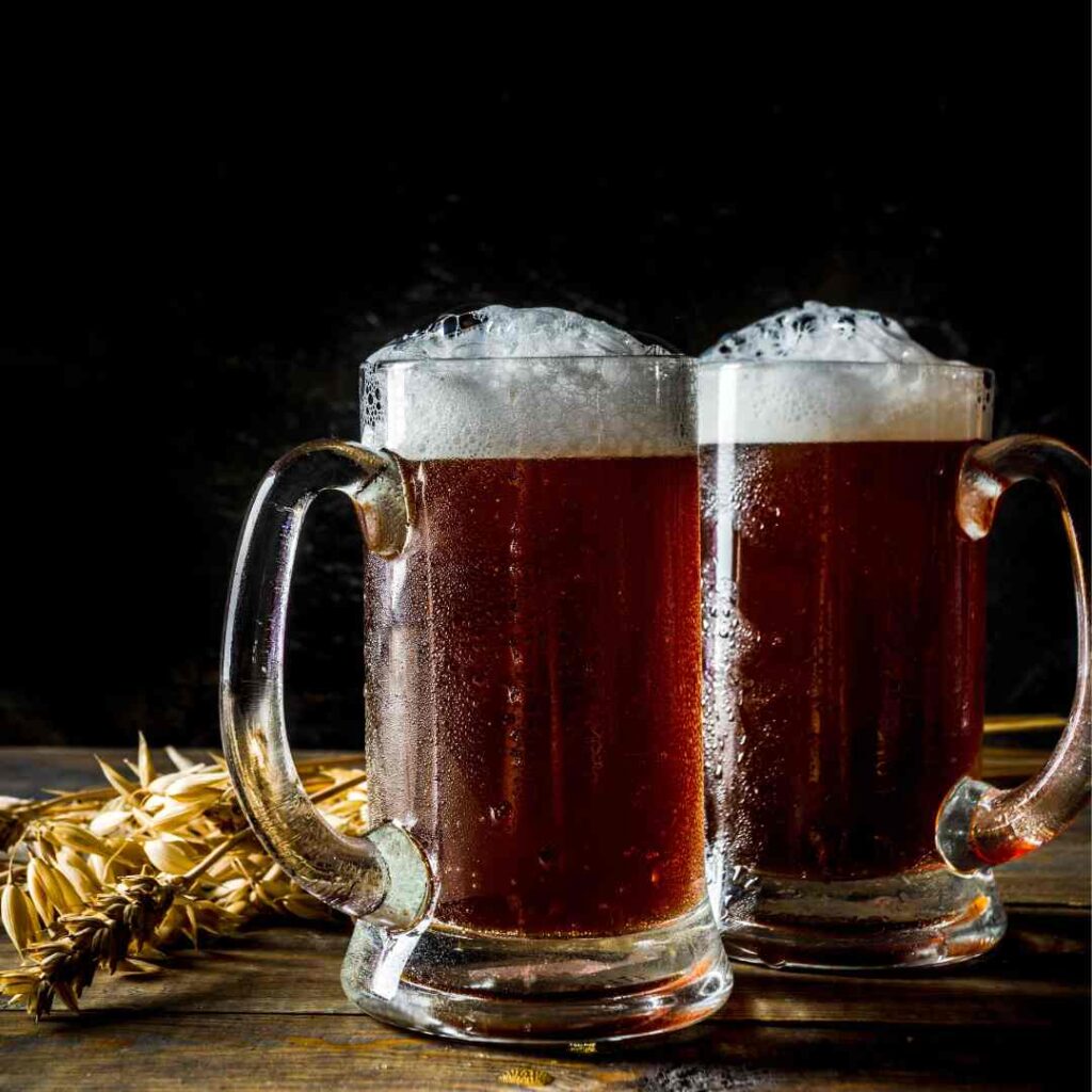 2 German alt biers on  a table with barley and hops